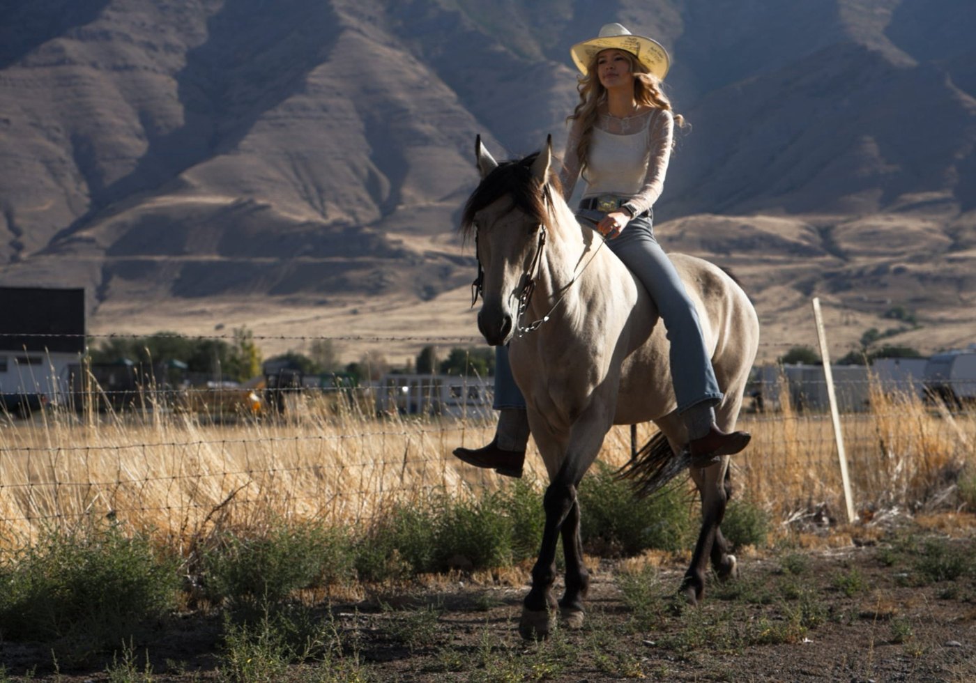 Kennedy riding her buckskin through a field below the mountains